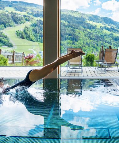 Schwimmer taucht ins Innenbecken; Berglandschaft sichtbar.