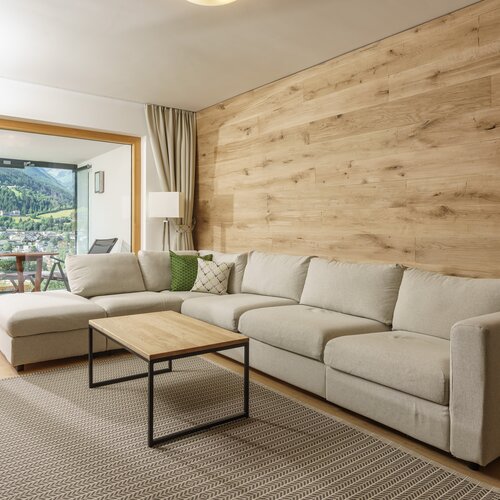 Modernes Wohnzimmer mit beigem Ecksofa, Holzverkleidung und Balkonblick