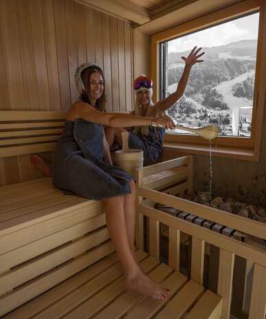 Zwei Frauen in einer Holzsauna, Wasser gießend