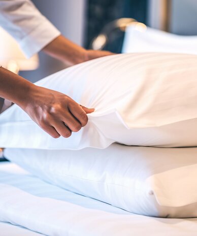 Person richtet Kissen auf einem ordentlich bezogenen Bett.