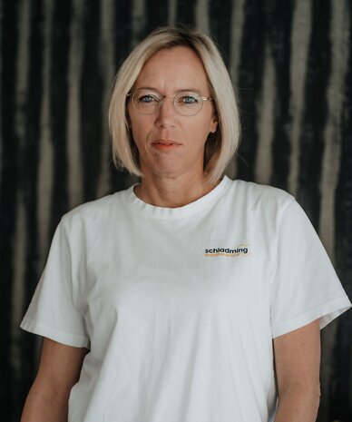Porträt einer Frau mit kurzen blonden Haaren, Brille und weißem T-Shirt