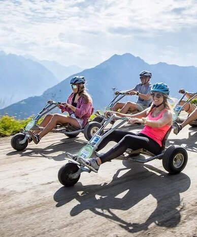 Gruppe von vier Personen mit Helmen fährt Pedal-Go-Karts auf Bergstraße