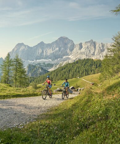 Zwei Radfahrer fahren auf grobem Gravelweg durch alpine Landschaft