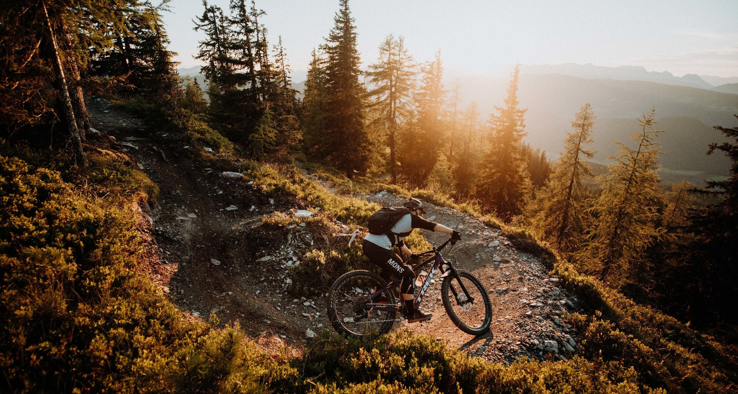Mountainbiker auf felsigem Waldweg bei Sonnenuntergang
