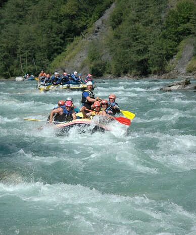 Rafting-Gruppe trägt Helme und Schwimmwesten auf einem turbulenten Fluss