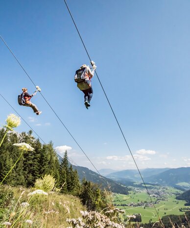Gruppe von Menschen beim Seilrutschen über ein Bergtal