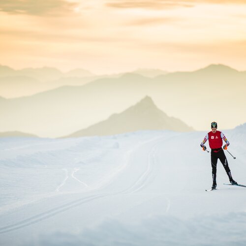 Skifahrer in roter Weste fährt auf verschneiter Piste beim Sonnenuntergang | © Photographer: Dominik Steiner