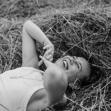 Junge Frau liegt lachend im Heu im Freien