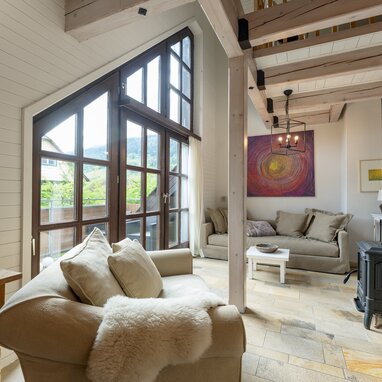 Sunlit living room with large wooden-framed windows and beams