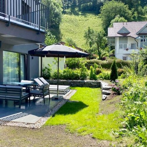 Modernes Haus mit Terrasse, Sitzbereich, Sonnenschirm und Garten.