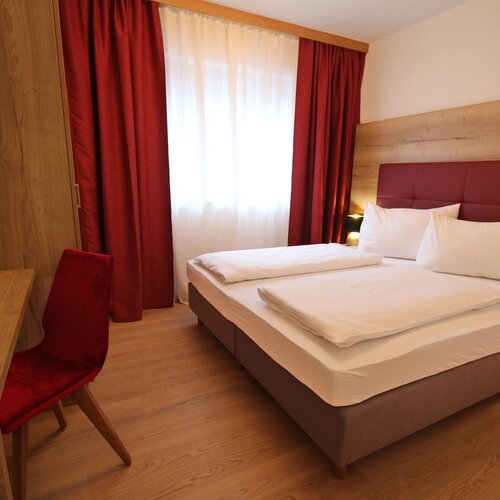 Hotelzimmer mit Doppelbett, rotem Kopfteil und Holzmöbeln.