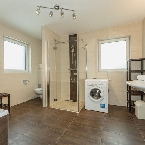 Modernes Badezimmer mit Glasdusche, Toilette, Waschbecken, Waschmaschine.