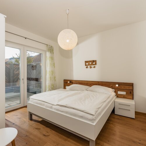 Helles Schlafzimmer mit weißer Wand, Holz-Kopfteil und Glastüren