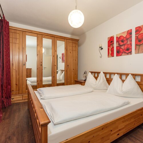 Holzbett mit weißer Bettwäsche, Spiegelkleiderschrank und pinken Vorhängen