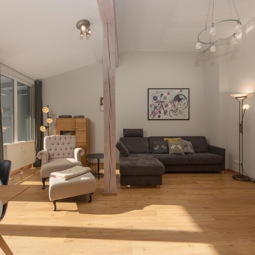 Helles Wohnzimmer mit grauem Sofa, Sesseln und großen Fenstern.