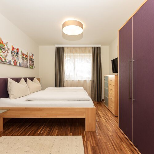 Hotelzimmer mit großem Bett, lila Kleiderschrank und Katzenkunst