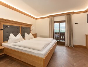 Hotelzimmer mit Holzbett, weißer Bettwäsche und Balkonblick.