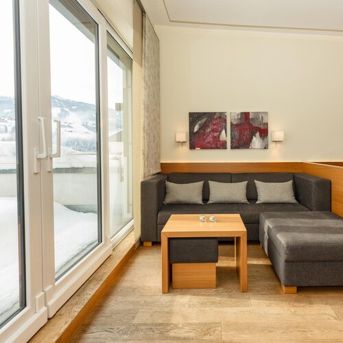 Helles Hotel-Wohnzimmer mit grauer Couch und Schnee draußen