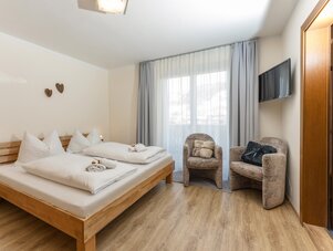 Holzbett mit weißer Bettwäsche und zwei Sesseln am Fenster