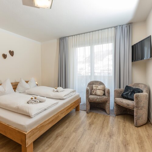 Holzbett mit weißer Bettwäsche und zwei Sesseln am Fenster