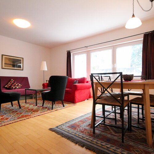 Wohnzimmer mit lila Sofa, rotem Sessel und buntem Teppich. | © SCHLADMING-APPARTEMENTS