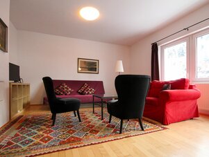 Wohnzimmer mit roter Couch, zwei schwarzen Sesseln, bunter Teppich | © SCHLADMING-APPARTEMENTS