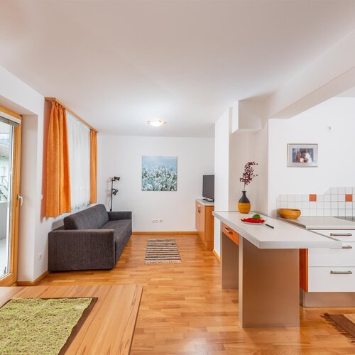 Offen gestalteter Wohnbereich mit grauem Sofa und Kücheninsel.