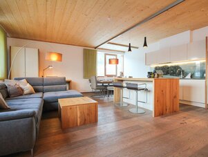 Offener Wohnbereich mit blauem Sofa, Holzdecke und Kücheninsel | © SCHLADMING-APPARTEMENTS