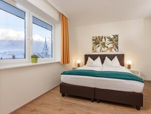 Helles Hotelzimmer mit Doppelbett, großen Fenstern und Bergblick