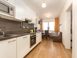 Moderne Küche mit weißen Schränken und Essbereich am Fenster.