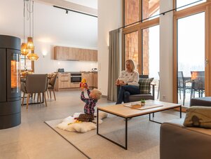 Kind spielt mit Spielzeug auf flauschigem Teppich, Frau sitzt daneben