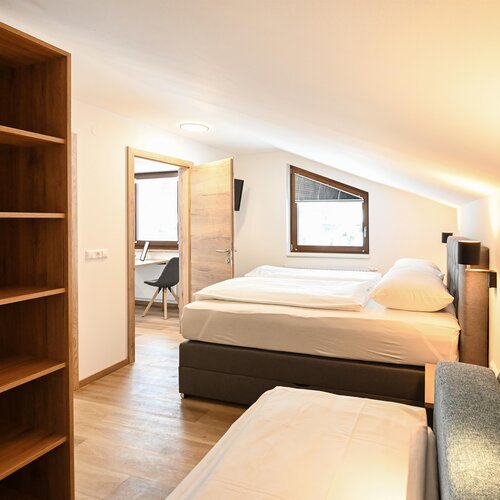 Schlafzimmer mit zwei Betten, Holzregal und Arbeitsbereich