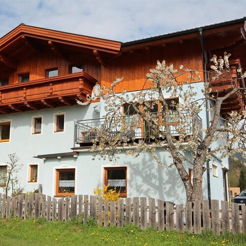 Zweistöckiges Haus mit Holzoberteil und blühendem Baum im Vorgarten