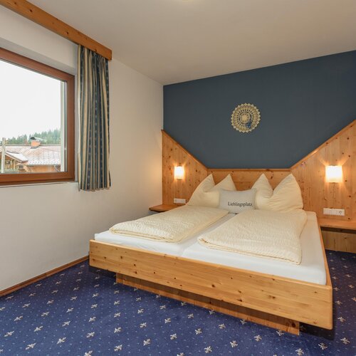 Gemütliches Schlafzimmer aus Holz mit blauer Akzentwand; Kissen mit Aufdruck 'Lieblingsplatz'.