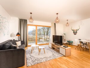 Helles Wohnzimmer mit grauem Sofa, Holzboden, Teppich und Balkonblick