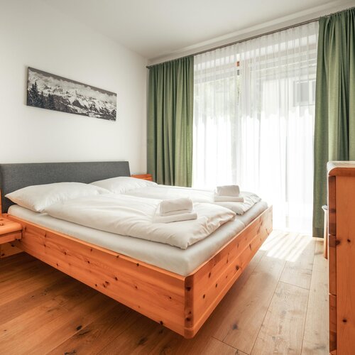 Holzplattformbett mit weißer Bettwäsche in hellem Zimmer | © TIEBER