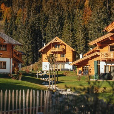Row of wooden alpine chalets beside green lawn and trees