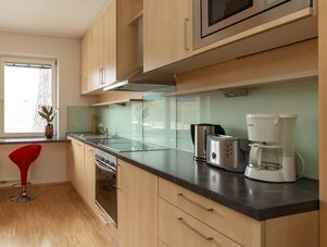 Moderne Küche mit hellen Holzmöbeln, Glasrückwand und Geräten