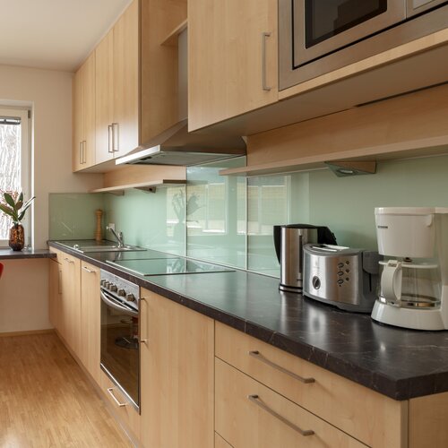 Moderne Küche mit hellen Holzmöbeln, Glasrückwand und Geräten