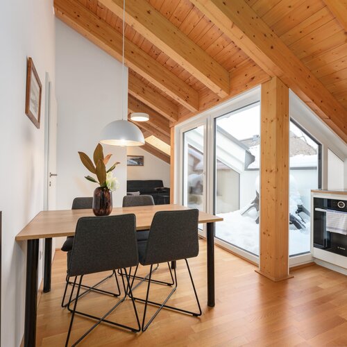 Essbereich mit Holzbalken, großen Fenstern und Vase