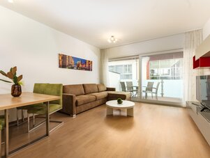 Geräumiges Wohnzimmer mit brauner Couch, grünen Stühlen, Balkonzugang