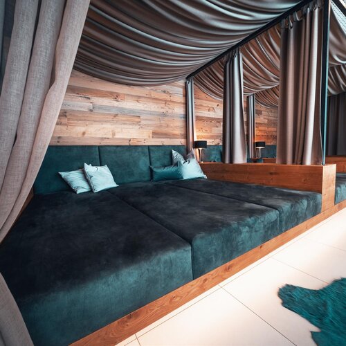 Loungebereich mit tealfarbigem Samt-Ecksofa und Vorhängen