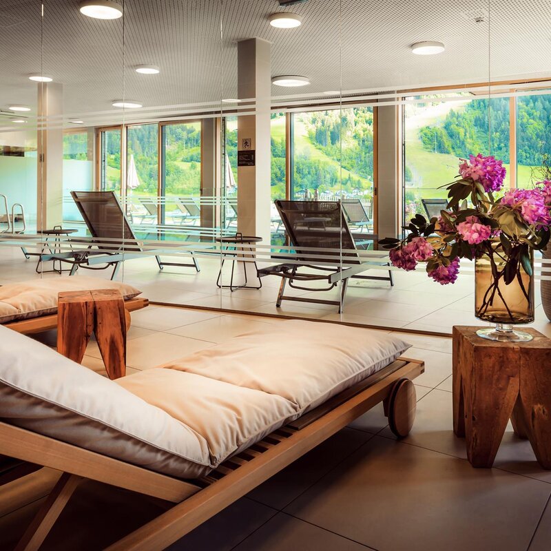 Spa lounge with wooden sun loungers, cushions, and glass partition