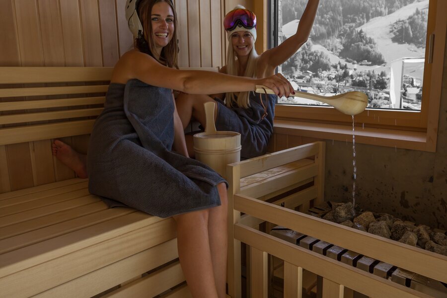 Zwei Frauen in einer Holzsauna, Wasser gießend
