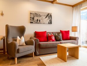 Gemütliches Wohnzimmer mit grauer Couch, Sessel und roten Kissen