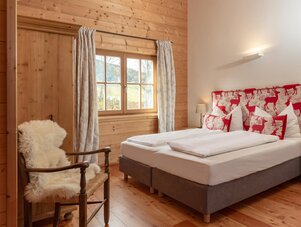 Gemütliches holzverkleidetes Schlafzimmer mit Hirschmuster-Kopfteil und weißer Bettwäsche