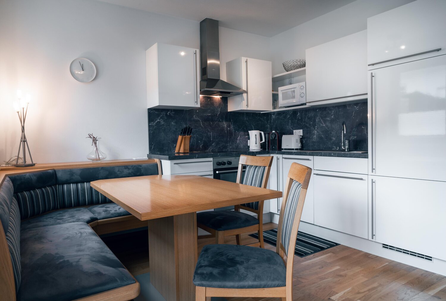 Moderne Küche mit weißen Schränken, dunkler Marmorrückwand und Esstisch