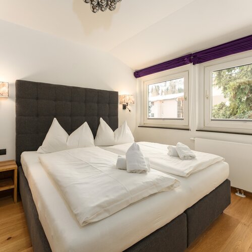 Großes Doppelbett mit weißen Laken und gepolstertem Kopfteil