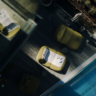 Luftaufnahme einer Poolterrasse mit grünen Loungesesseln und Magazinen