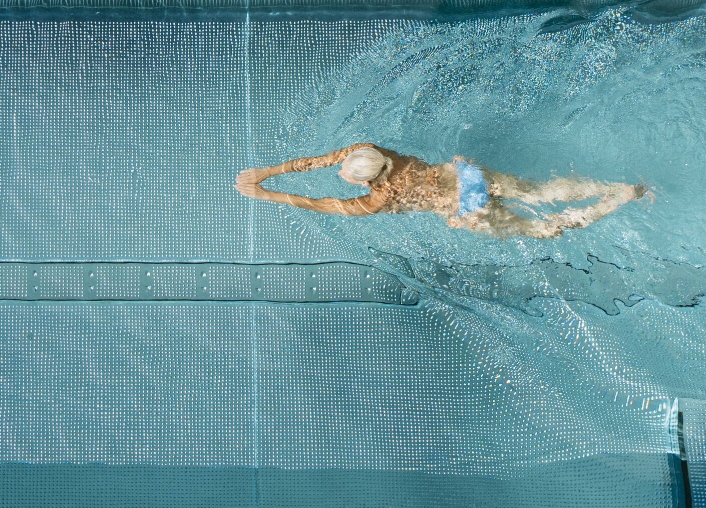 Luftaufnahme eines Poolbeckens mit Schwimmer und Liegen am Beckenrand.